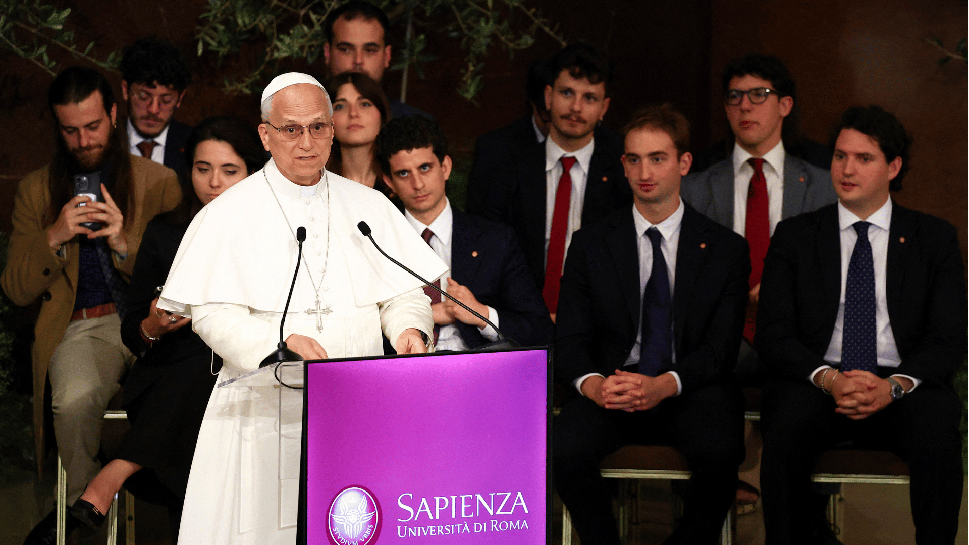 Papa Leão XIV discursa em púlpito da Universidade Sapienza de Roma diante de estudantes e autoridades acadêmicas durante visita pastoral.