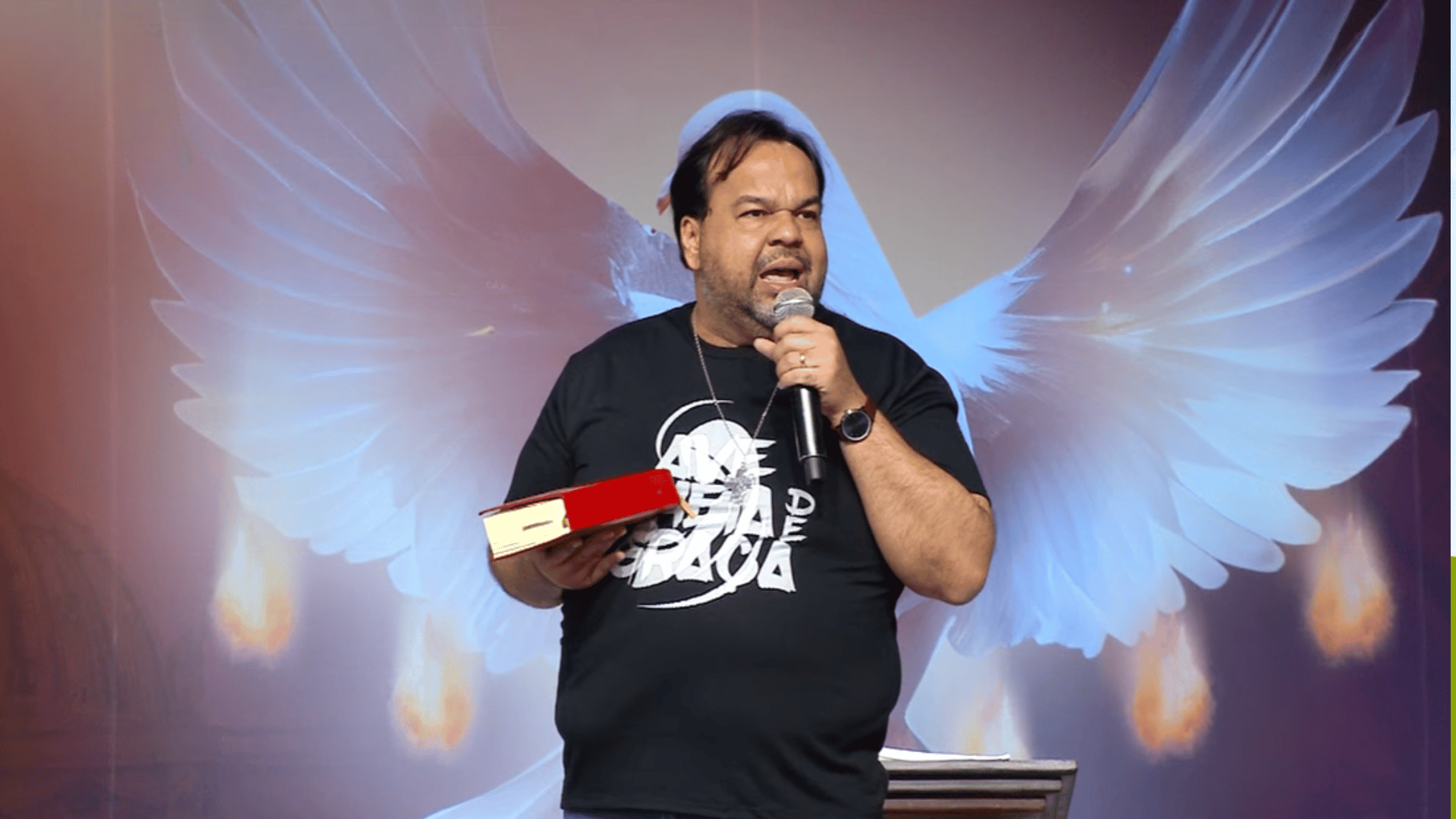 O pregador Moisés Rocha veste uma camiseta preta, segura um microfone com uma mão e a bíblia com a outra