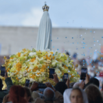 A imagem mostra a imagem de Nossa Senhora de Fátima em cima do andor, de costas, e a multidão ao redor