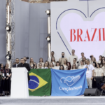 A imagem mostra várias pessoas em cima de um palco. Etre elas, está o presidente da Canção Nova, padre Wagner Ferreira, e demais missionários da comunidade que seguram uma bandeira do Brasil e uma bandeira azul com a logo da Canção Nova