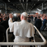 O Papa Leão XIV aparece com suas habituais vestes brancas em pé no papamóvel acenando para uma multidão de pessoas