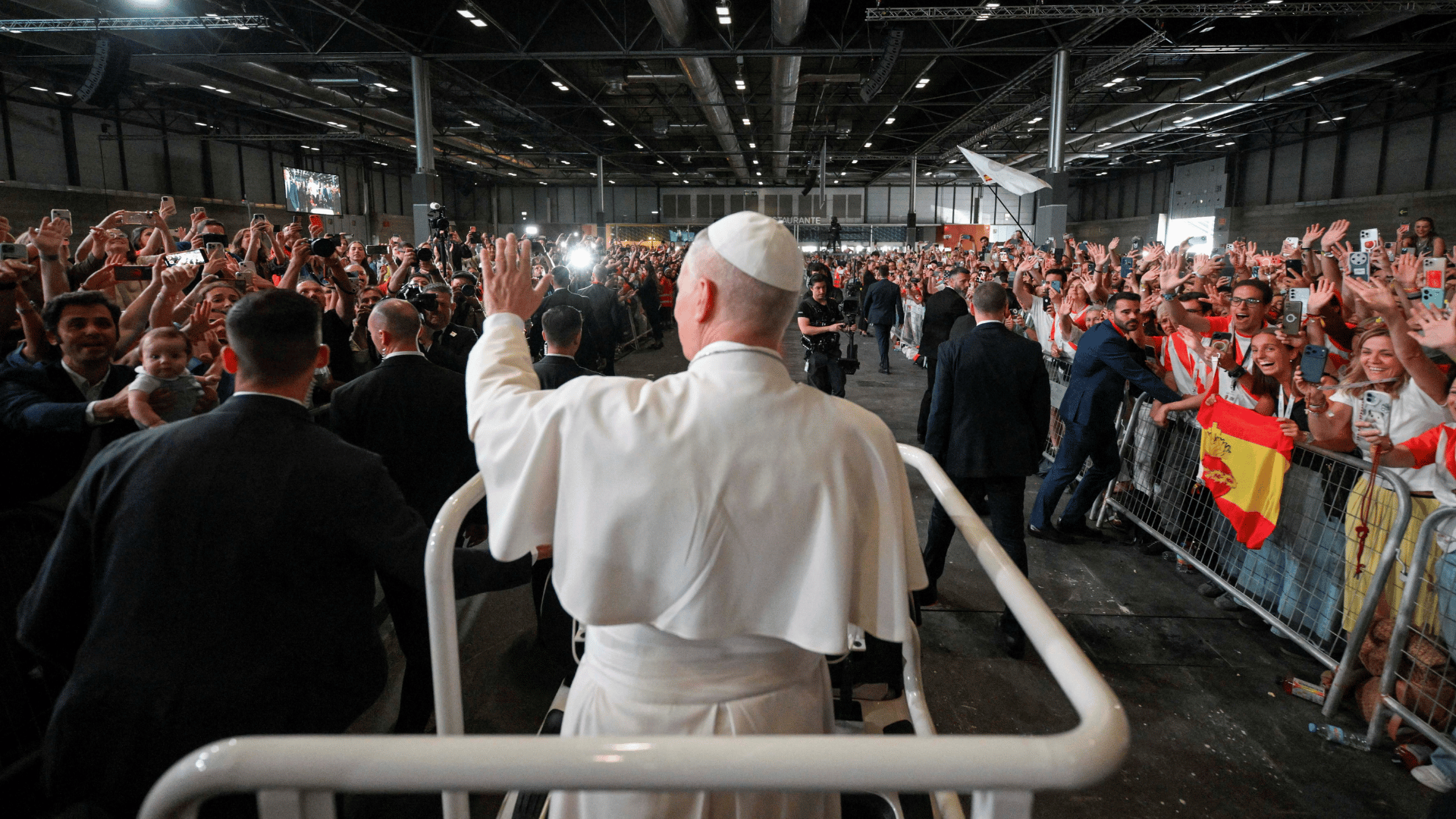 O Papa Leão XIV aparece com suas habituais vestes brancas em pé no papamóvel acenando para uma multidão de pessoas