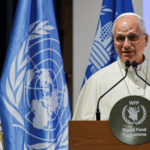 Papa discursa no púlpito do Programa Mundial de Alimentos (WFP) da ONU, com as bandeiras do Vaticano e das Nações Unidas ao fundo.