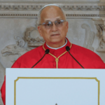 A imagem mostra o Papa Leão XIV com a moseta vermelha à frente de um púlpito com dois microfones