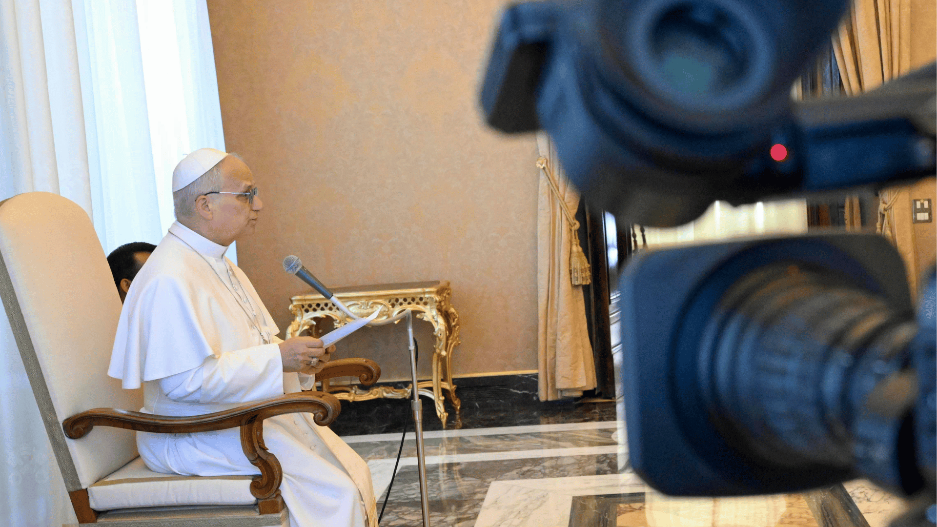 Papa Leão XIV em audiência no Vaticano. Sentado e com documentos em mãos, o Pontífice fala ao microfone enquanto câmeras registram a audiência.