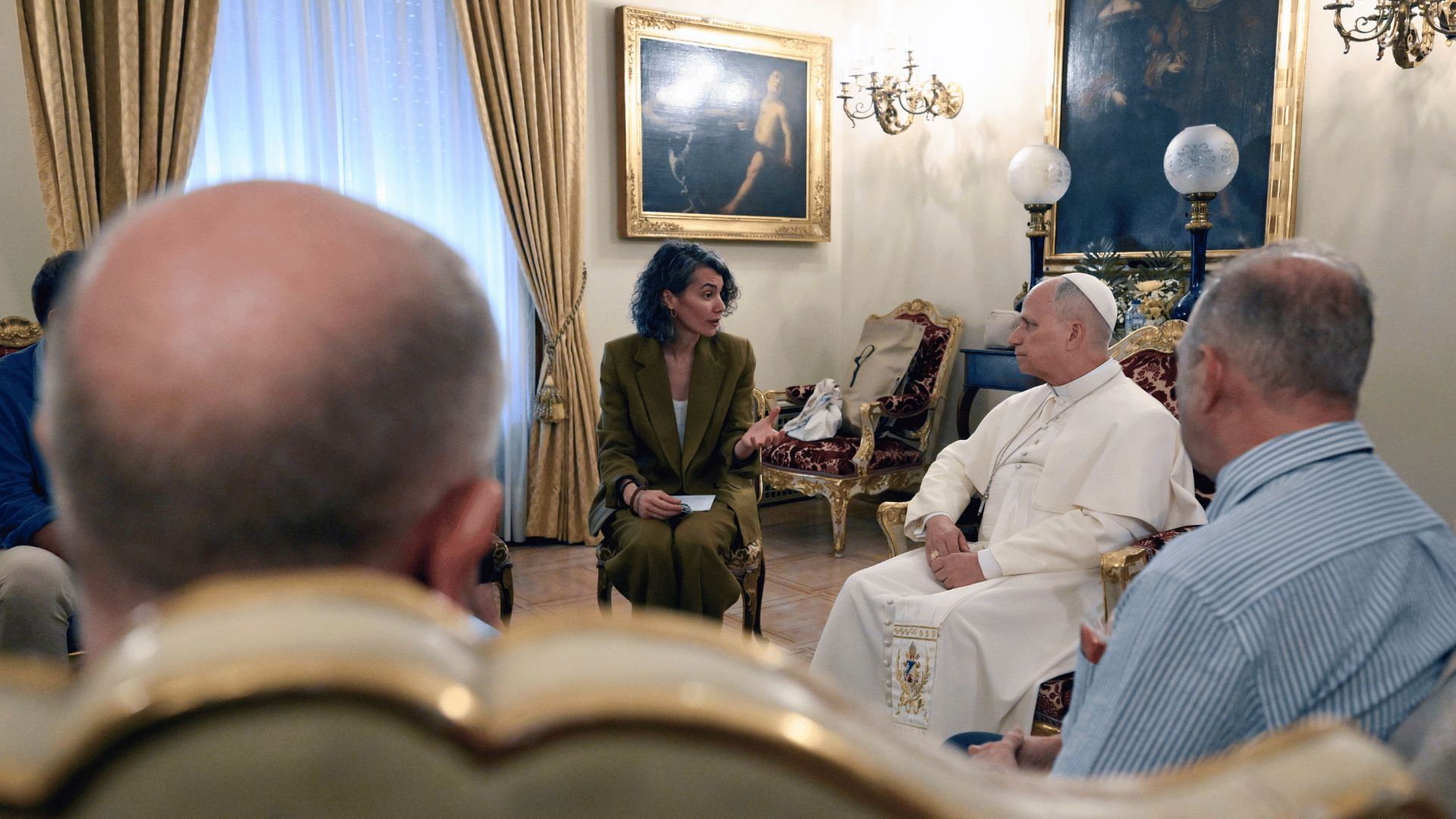 O Papa Leão XIV aparece sentado com pessoas também sentadas ao seu redor. Eles estão eu uma sala com alguns quadros na parede. É a nunciatura apostólica em Madri