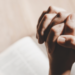 Mãos entrelaçadas em oração sobre uma Bíblia aberta, simbolizando um momento de fé, meditação e leitura da Palavra de Deus.