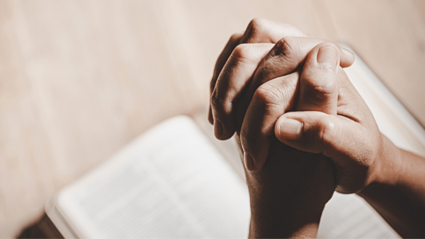 Mãos entrelaçadas em oração sobre uma Bíblia aberta, simbolizando um momento de fé, meditação e leitura da Palavra de Deus.