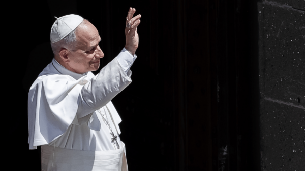 Papa Leão XIV acena aos fiéis enquanto deixa um edifício durante seu período de descanso em Castel Gandolfo, usando veste branca e solidéu.