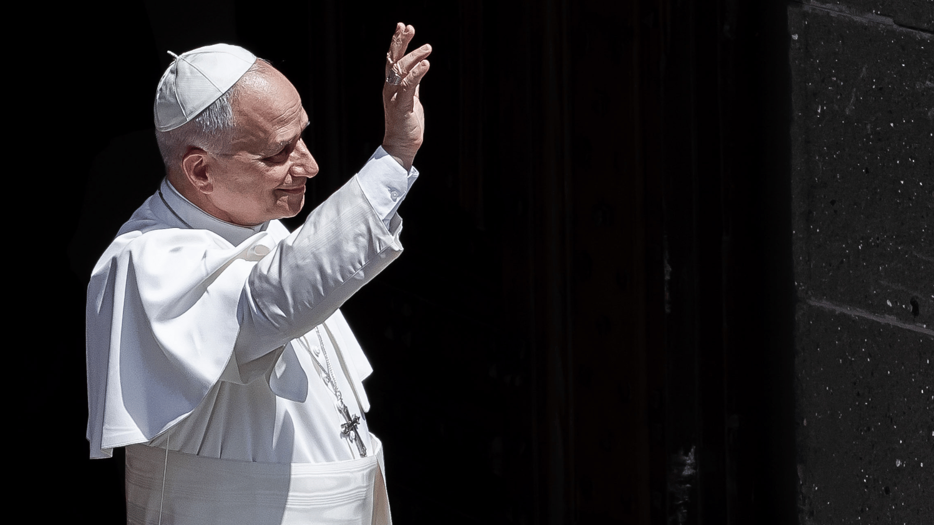 Papa Leão XIV acena aos fiéis enquanto deixa um edifício durante seu período de descanso em Castel Gandolfo, usando veste branca e solidéu.