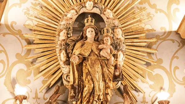 Imagem de Nossa Senhora do Carmo com o Menino Jesus ao colo, ambos coroados, tendo ao fundo um resplendor dourado cercado por anjos. A Virgem segura o escapulário, símbolo da devoção carmelita.