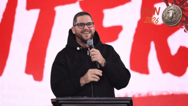 Padre Ailton fala ao público durante pregação no PHN 2026, segurando um microfone e sorrindo diante do palco principal do evento.