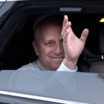 O Papa Leão XIV acena de dentro de um carro preto, com a janela abaixada.