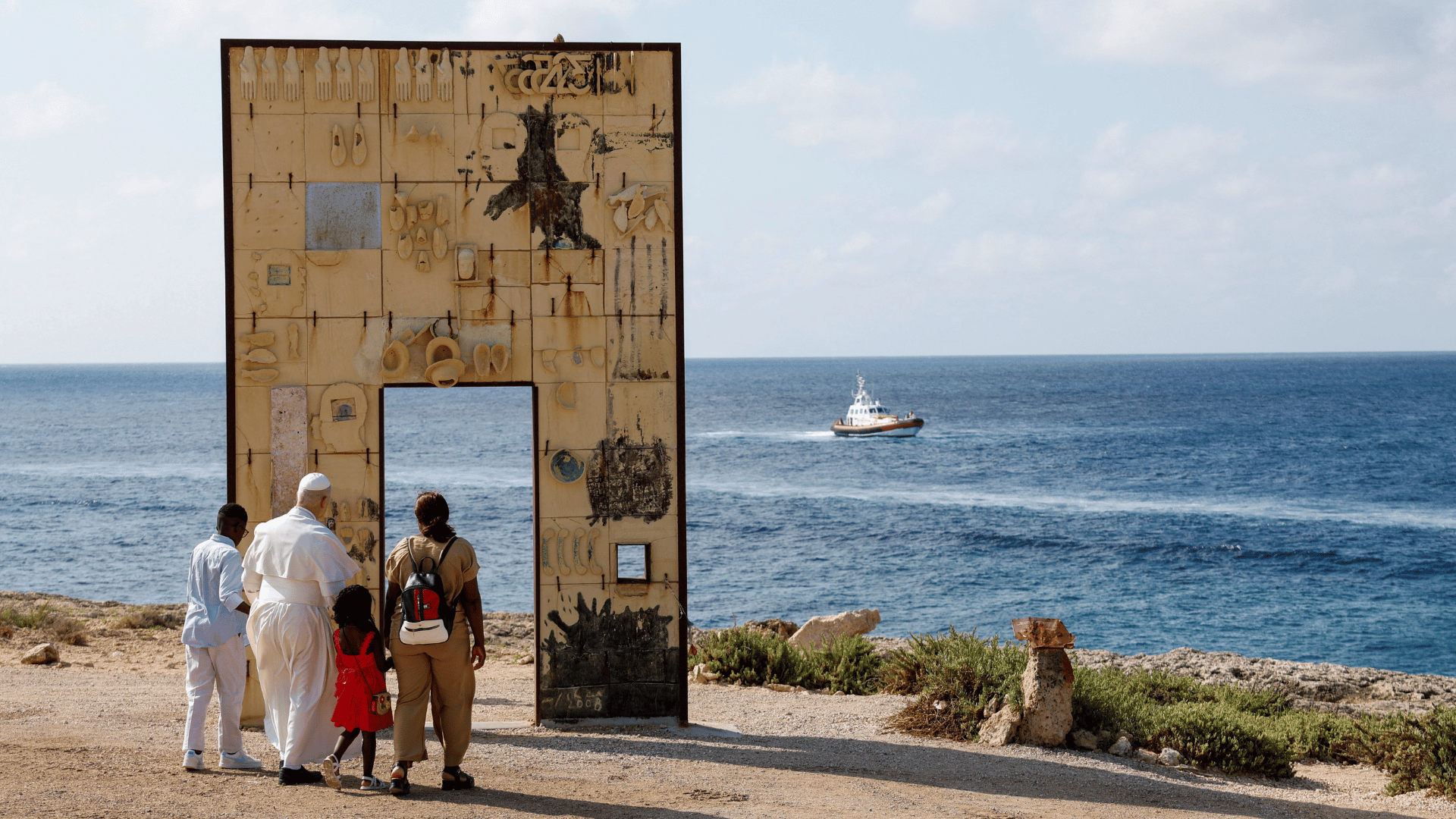 Papa Leão XIV visita a Porta da Europa junto a família de migrantes A imagem ilustra o Papa Leão XIV, com suas habituais vestes pontifícias, junto a uma família de migrantes. Eles visitam um monumento intitulado "Porta da Europa", que consiste em um grande pórtico com vista para o Mar Mediterrâneo, presente no fundo da imagem.