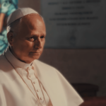 Papa Leão XIV em momento de oração dentro de uma igreja, com vitral ao fundo e expressão serena.