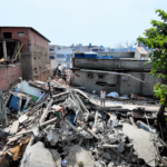 Área destruída por terremoto em La Guaira, na Venezuela, com edifícios desabados, equipes e moradores sobre os escombros durante as buscas por vítimas.