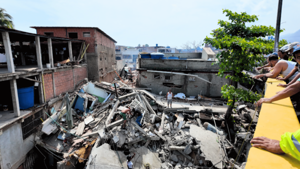 Área destruída por terremoto em La Guaira, na Venezuela, com edifícios desabados, equipes e moradores sobre os escombros durante as buscas por vítimas.