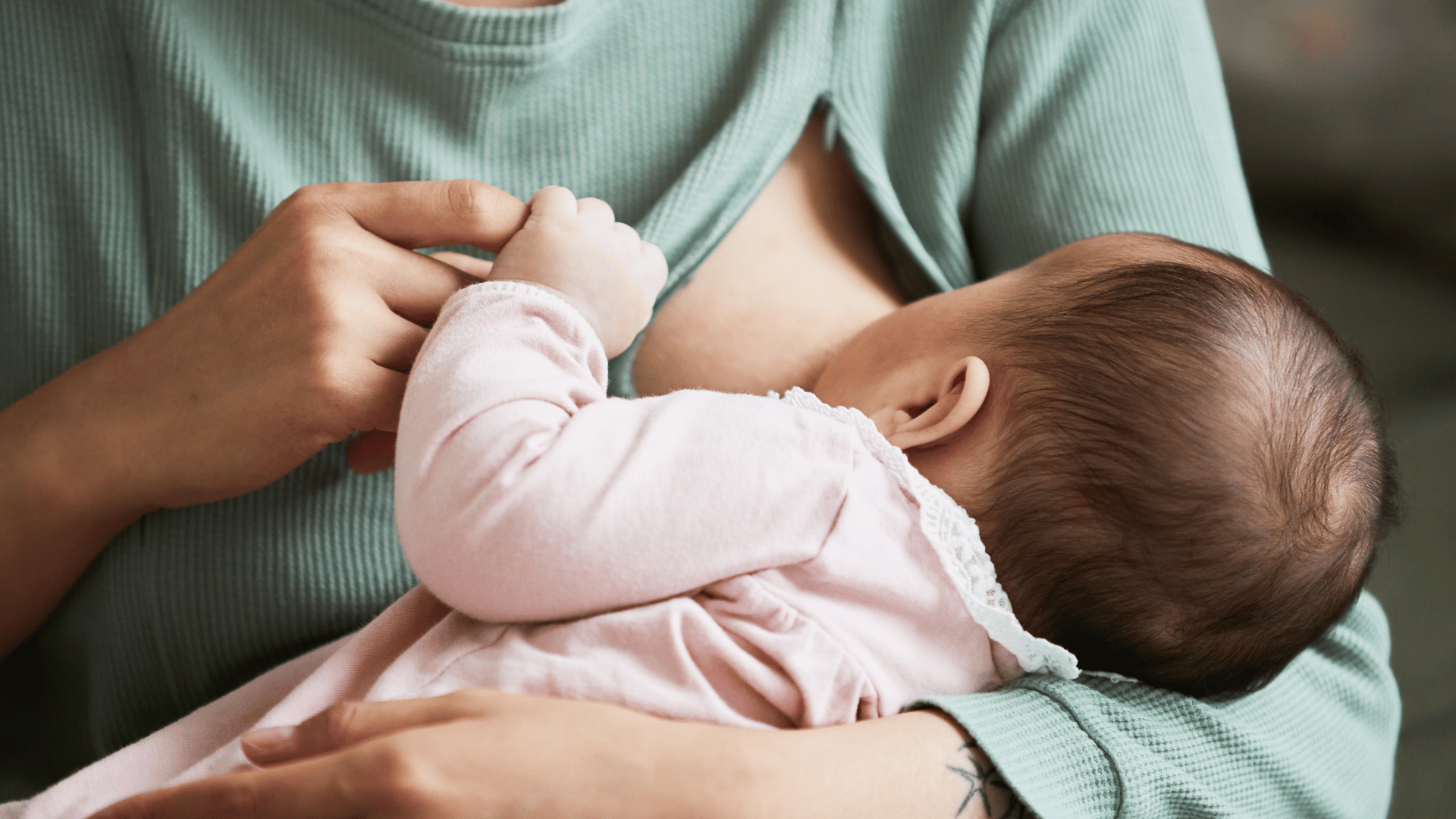 A foto mostra uma mulher segurando um bebê no colo, acariciando uma de suas mãozinhas e amamentando este bebê