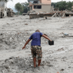 A imagem mostra um homem caminhando pela lama em meio a um cenário de destruição após inundações no Nepal