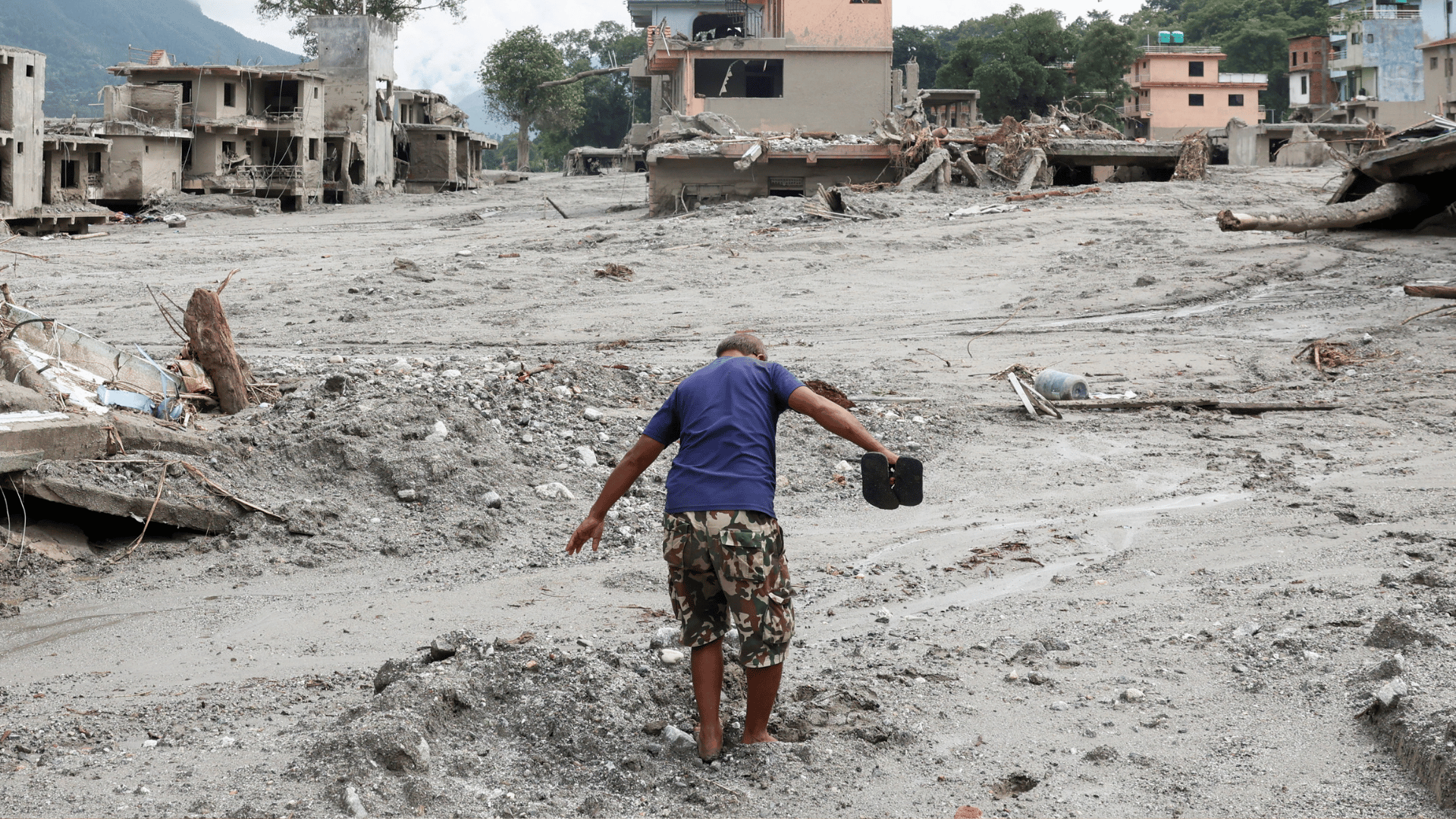 A imagem mostra um homem caminhando pela lama em meio a um cenário de destruição após inundações no Nepal