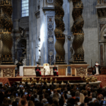 A imagem mostra, em plano aberto, a Basílica de São Pedro. No altar, está o Papa sentado e uma cadeira e dois clérigos sentados ao seu lado. Diante deles, estão os fiéis.