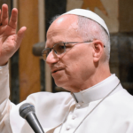 apa Leão XIV, usando vestes brancas e óculos, com os braços erguidos durante audiência no Vaticano.