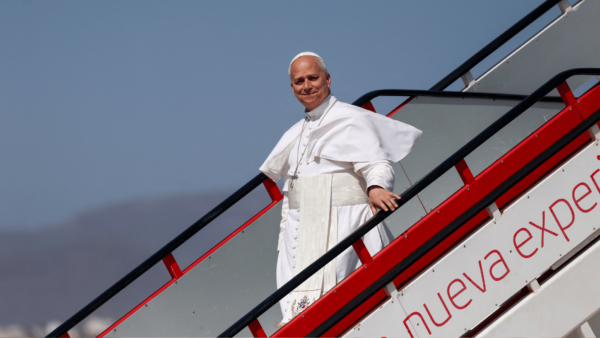 Papa Leão XIV desce a escada da aeronave ao chegar para uma viagem apostólica, vestido de branco e sorrindo para os presentes.