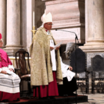 Patriarca de Lisboa, paramentado liturgicamente, fala ao microfone em ambiente interno do Mosteiro dos Jerônimos.