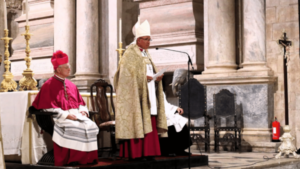 Patriarca de Lisboa, paramentado liturgicamente, fala ao microfone em ambiente interno do Mosteiro dos Jerônimos.