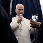 A imagem mostra o Papa Leão XIV em pé dentro do avião. Ele segura um microfone e fala aos jornalistas que o acompanham no voo.