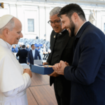 A imagem mostra o padre Roger Luis e o padre Donizete Heleno em pé, diante do Papa Leão XIV, que também está em pé.