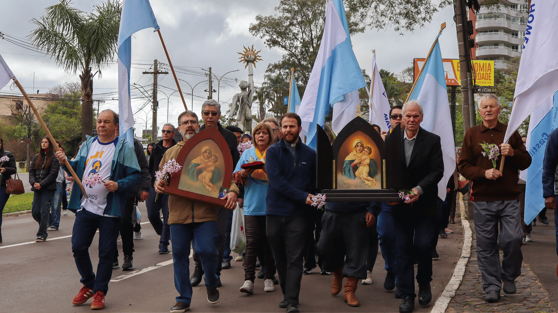 A imagem mostra um grupo de pessoas caminhando. Algumas delas carregam a imagem da Mãe Peregrina Três Vezes Admirável de Schoenstatt