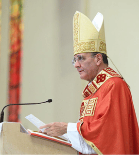 Dom Carlos Lema Garcia, com mitra e paramentos vermelhos, proclama a homilia durante celebração eucarística.