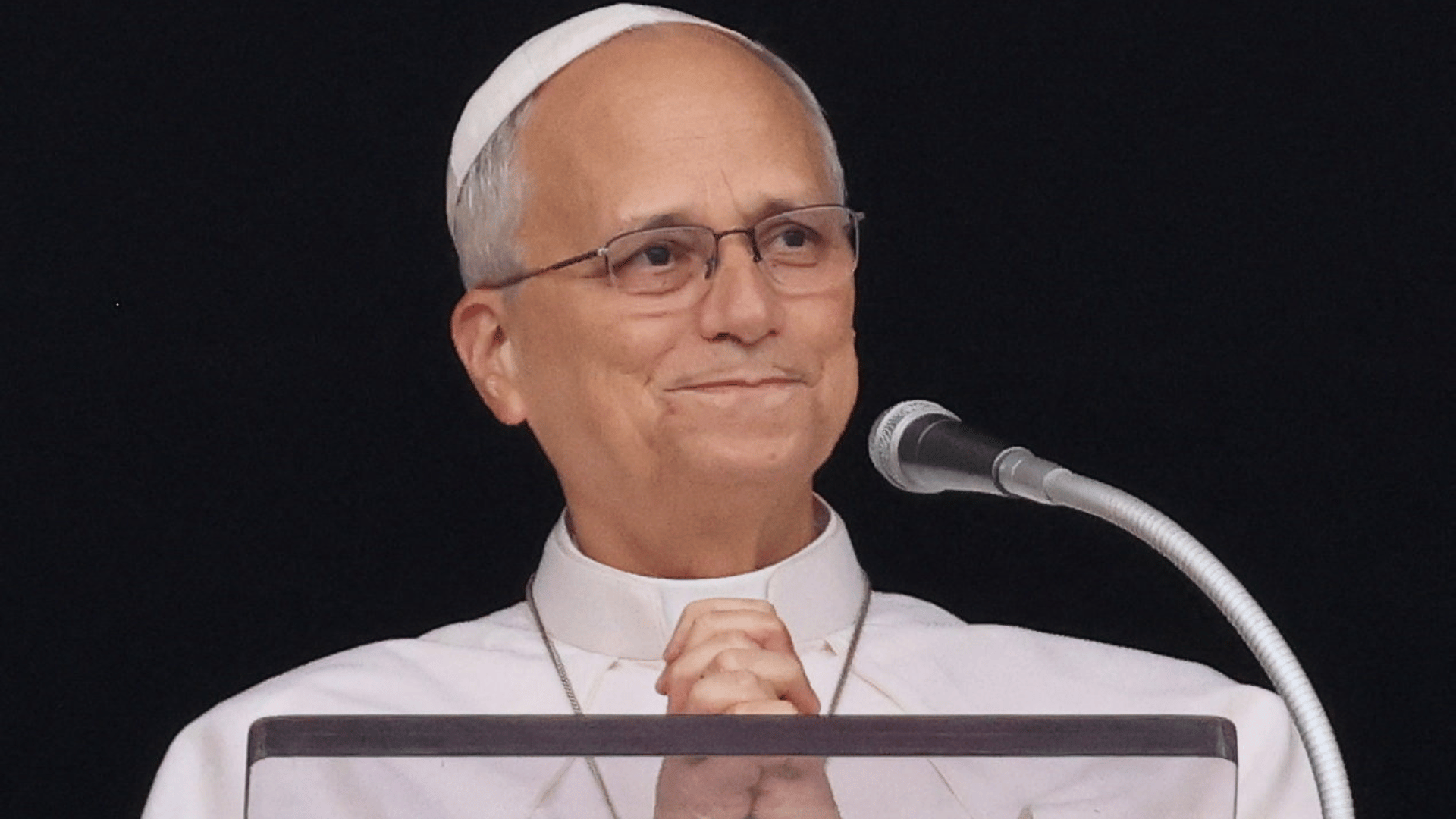 A imagem mostra o Papa Leão XIV sorrindo e apertando as mãos em posição de oração