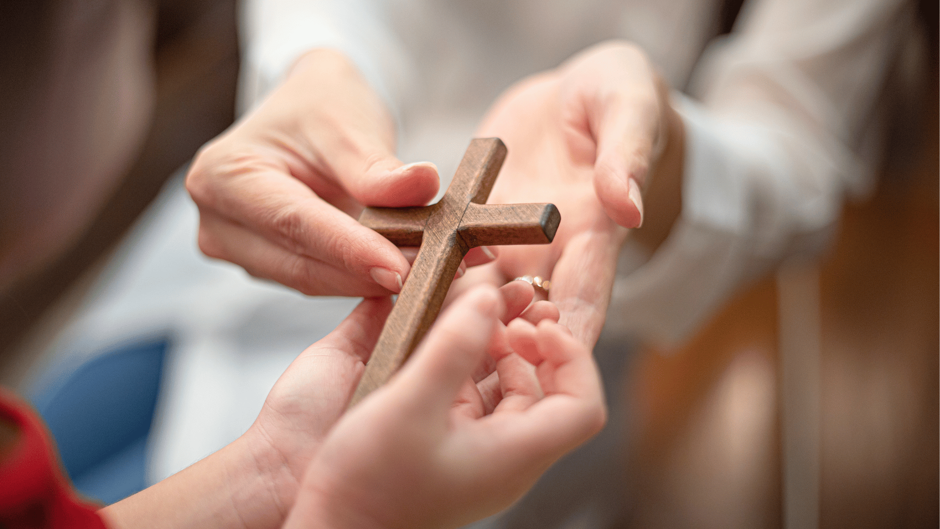 Mãos de um adulto entregam uma cruz de madeira às mãos de uma criança, simbolizando a transmissão da fé entre gerações.