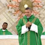 Sacertode com vestimenta verde e microfone na mão durante um sermão em uma Igreja