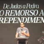 Pregador segurando microfone na mão, ao fundo escrito com o tema da pregação: "De Judas a Pedro do remorso ao arrependimento"
