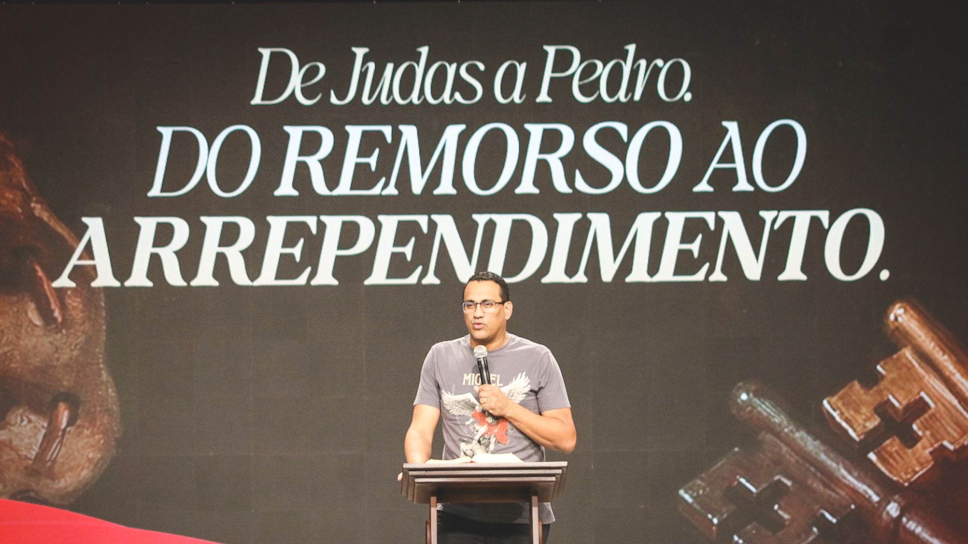 Pregador segurando microfone na mão, ao fundo escrito com o tema da pregação: "De Judas a Pedro do remorso ao arrependimento"