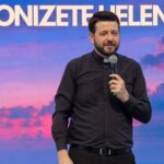 Sacerdote usando camisa de manga longa preta, com clergyman, segurando com uma das mãos o microfone enquanto palestra. Tema: "Eucaristia, Mistério anunciado no amor"