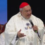 Dom Orani Tempesta, vestindo paramentos litúrgicos brancos e solidéu vermelho, fala ao microfone e gesticula durante uma celebração religiosa. Tema "Jesus, o Pão da Vida"