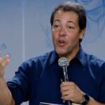 Homem segurando o microfone enquanto gesticula com uma das mãos. Tema: "Maria, a Mãe que intercede: Dai-nos a bênção!"