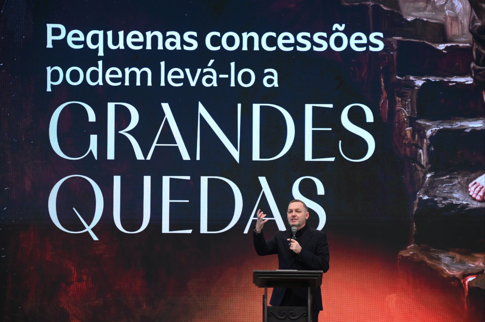 Homem usando blazer escura discursa num púlpito. Tema: "Pequenas concessões podem levá-lo a GRANDES QUEDAS"