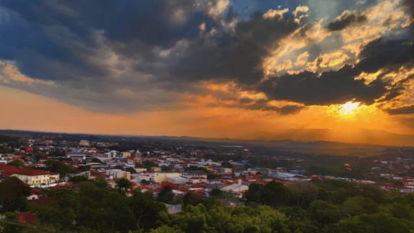 Vista panorâmica de uma cidade ao pôr do sol, com raios de luz dourada atravessando nuvens dramáticas e iluminações no horizonte, inspirando o momento de pedir perdão.