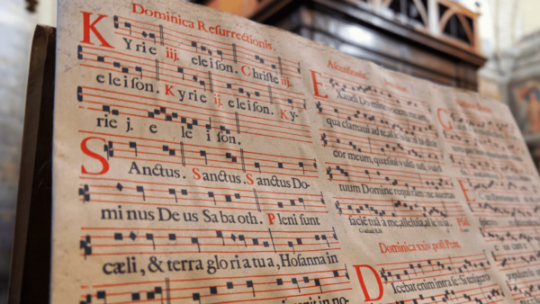 Esta imagem é um close-up (plano aproximado) de um grande livro litúrgico antigo aberto, focado nas páginas que contêm partituras de canto gregoriano.