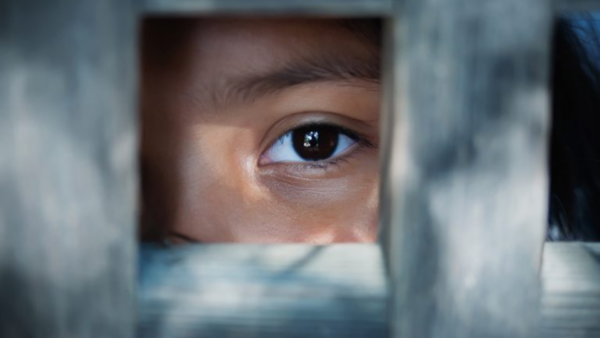Exploração sexual e tráfico de mulheres e criança Olho de uma criança visto por entre frestas de madeira, transmitindo sensação de vulnerabilidade e aprisionamento