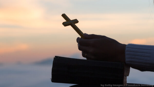 fé: Pessoa segurando um crucifixo dourado sobre uma Bíblia, em momento de oração ao pôr do sol.