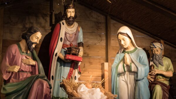 Uma cena detalhada de Natal com estátuas de São José, um Rei Mago, a Virgem Maria e outro Rei Mago ao redor do Menino Jesus em uma manjedoura de madeira.
