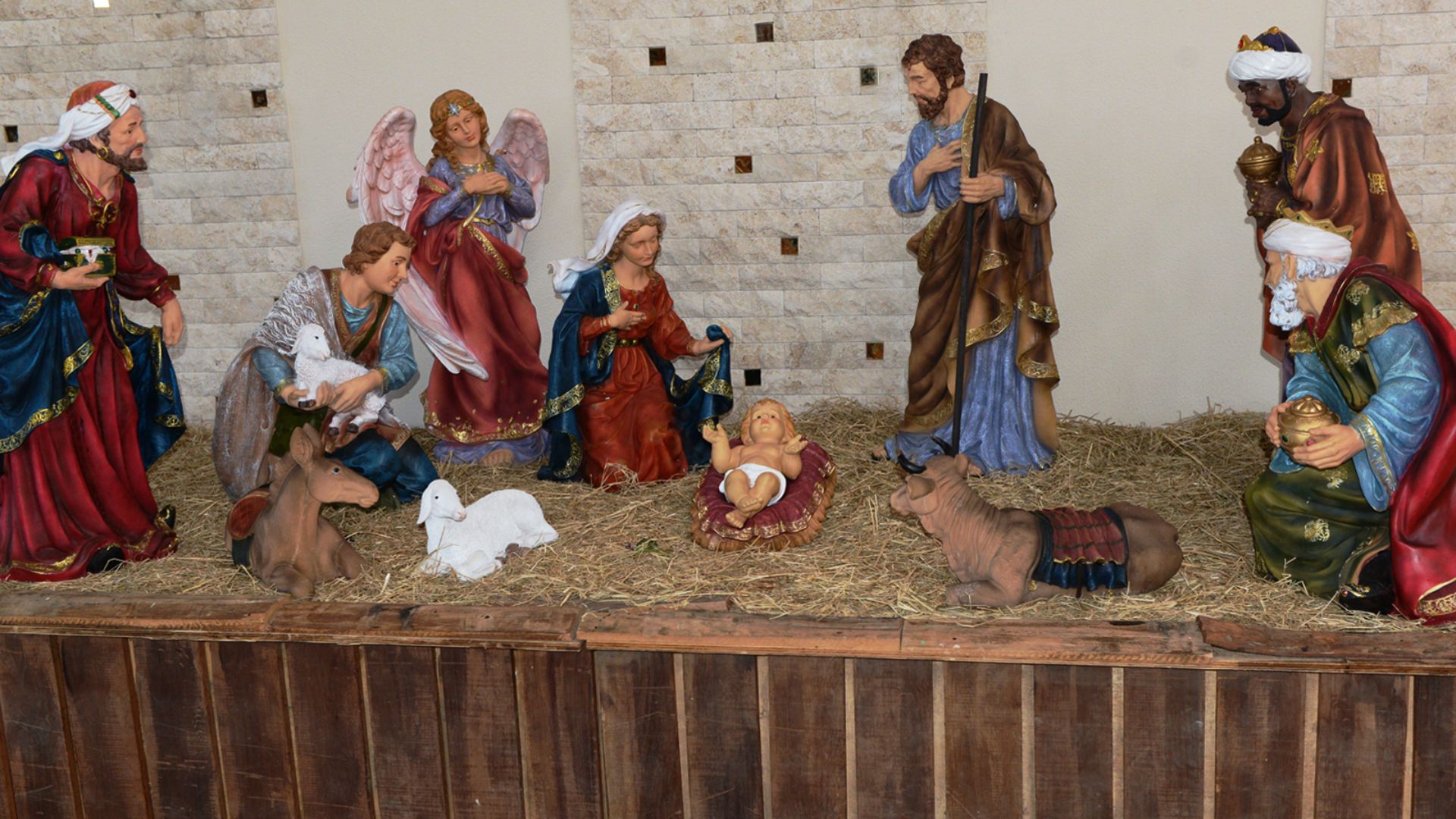 Presépio detalhado com figuras de Maria, José, Reis Magos e anjos ao redor do Menino Jesus deitado na palha seca.