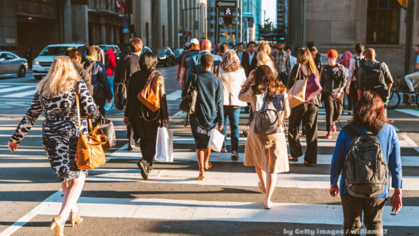 Multidão atravessa faixa de pedestres em cidade movimentada, refletindo o fluxo constante e caótico da vida urbana na sociedade contemporânea.