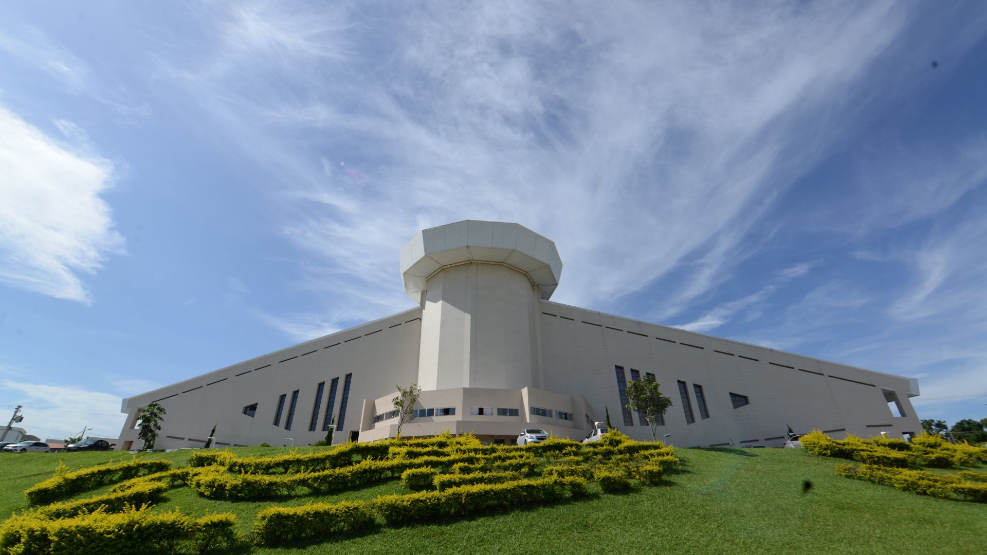 Fachada do Santuário do Pai das Misericórdias com céu azul e simbolo da canção nova na frente do gramado